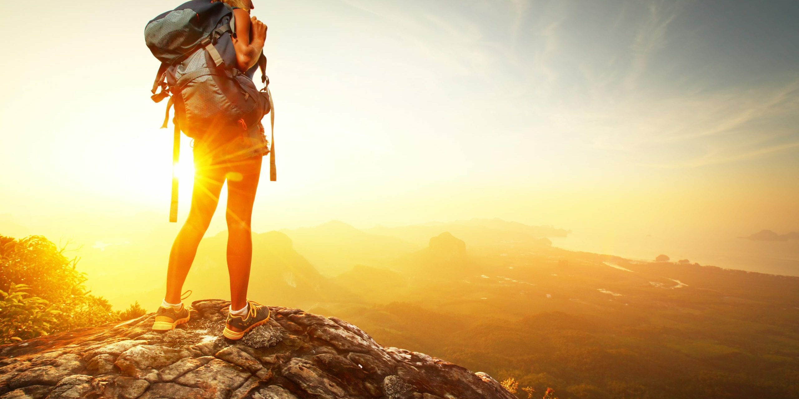 Hiker with backpack relaxing on top of a mountain and enjoying valley view during sunrise