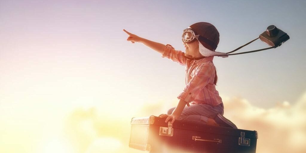 Dreams of travel! Child flying on a suitcase against the backdrop of a sunset.