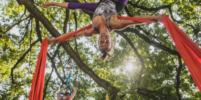 Aerial silk artist performing in sunny nature. Aerial silk artist performing movements on ropes hanging from trees on a sunny day in Tivoli park, Ljubljana.